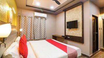 A hotel room with a bed, a ceiling fan, a TV mounted on the wall, and a shower area with patterned curtains.