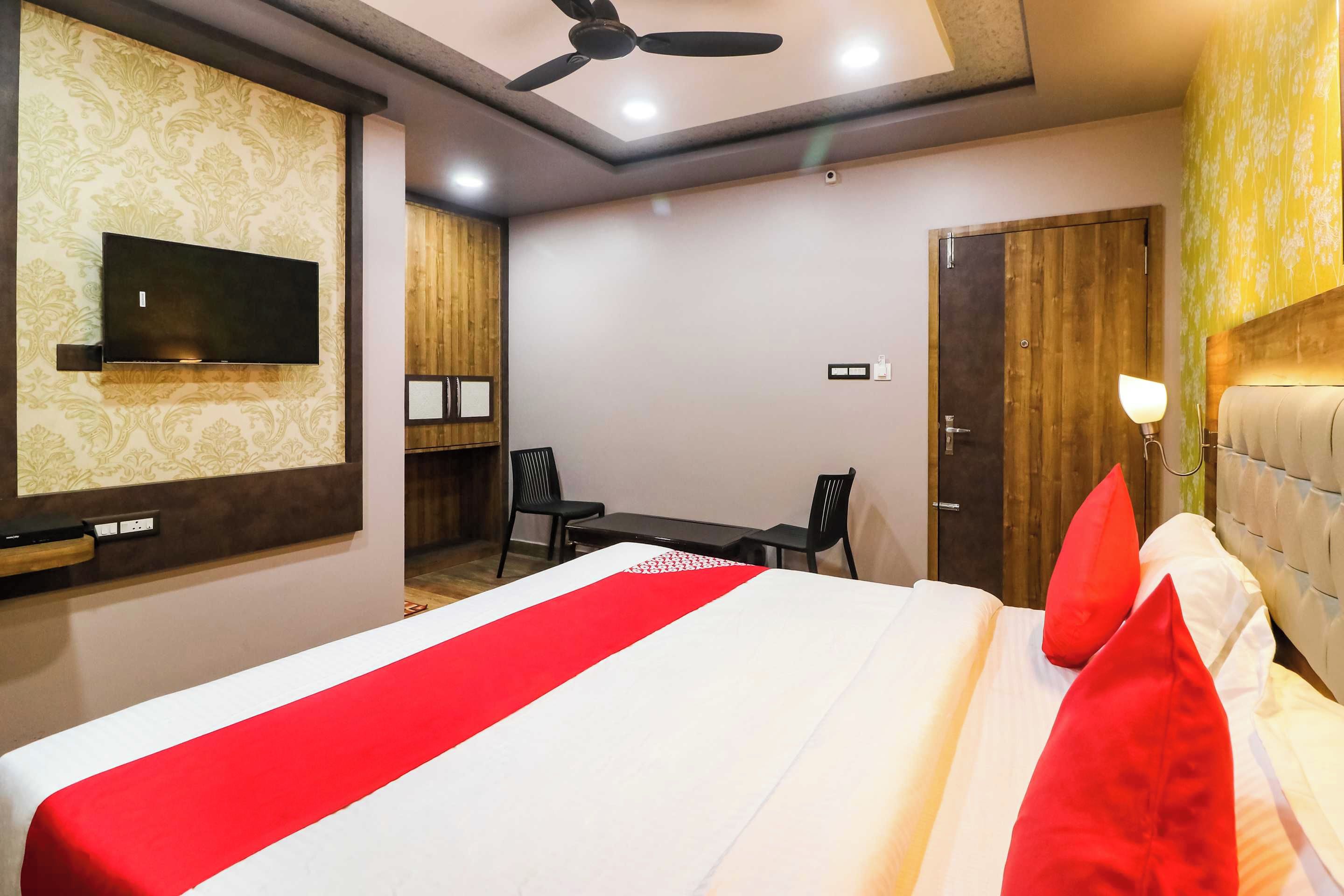 A hotel room with a bed, a desk, two chairs, a television, and a ceiling fan.
