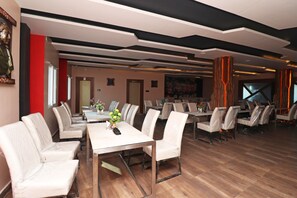 Comedor de hotel con varias mesas y sillas, suelo de madera y un diseño moderno en el techo.