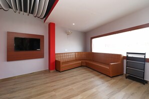 A room with a wooden floor, a brown leather sofa, a mounted TV, and a window with a view. - Hotel O Nirmalya Plaza (Behrampur)