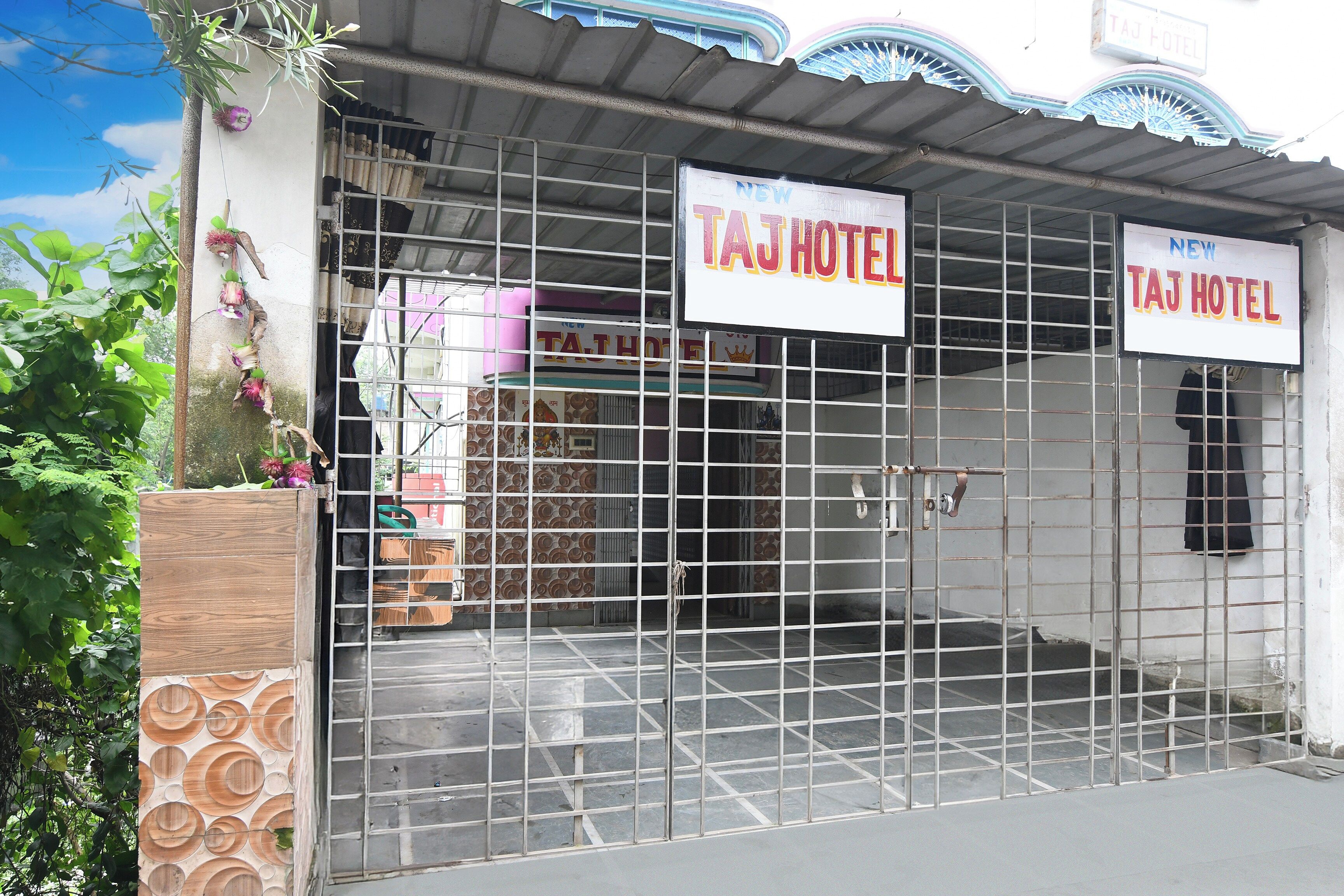 Une entrée fermée par un portail mène à un immeuble sur lequel on peut lire l’inscription « HÔTEL TAJ ».