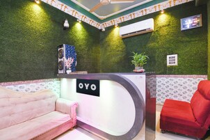 Una zona de recepción con pared verde, un mostrador blanco, un sofá rosa, una silla roja y una planta pequeña en maceta.