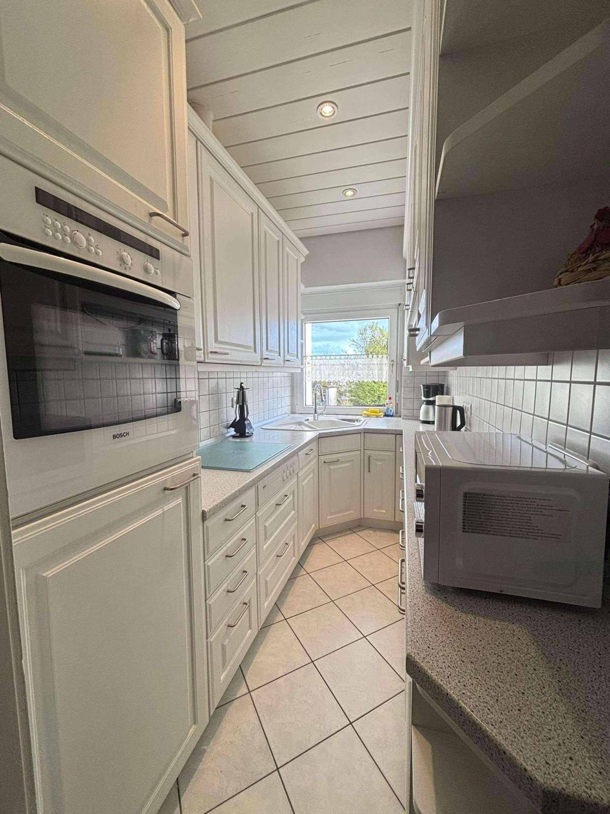 A kitchen with white cabinetry, a Bosch oven, a coffee maker, and a window providing natural light.