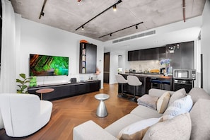 A modern living room with a sofa, a coffee table, and a TV. There is a kitchen area with a microwave and a sink. - Melbourne West End Escape (West Melbourne)