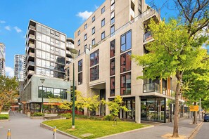 A modern multi-story building with a glass facade, a landscaped courtyard, and a restaurant named 'FOODWORKS' on the ground floor. - Melbourne West End Escape (West Melbourne)