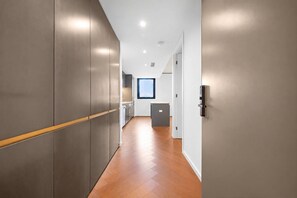 A modern hallway with a wooden floor, a kitchen area with a window, and a door with a handle. - Melbourne West End Escape (West Melbourne)