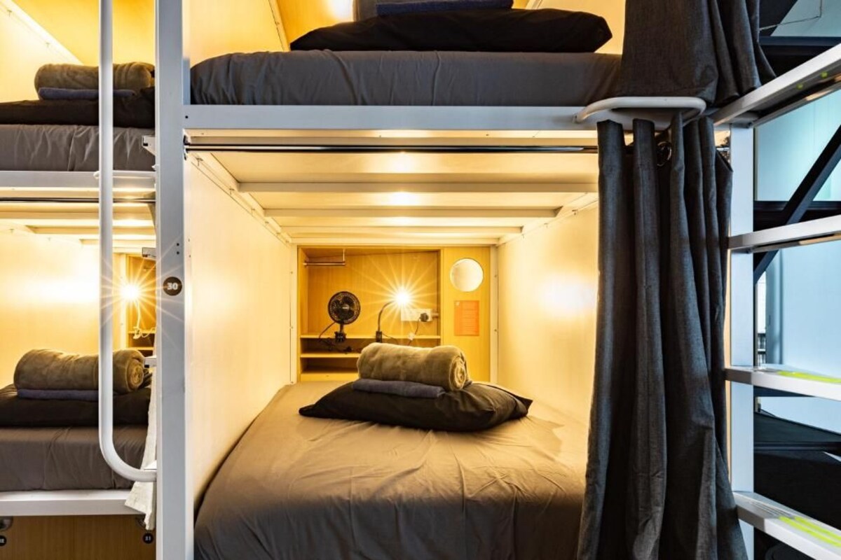 Et værelse med køjeseng, ventilator, lampe og et vindue med gardiner.