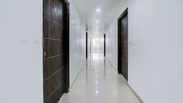 Un pasillo con puertas de madera oscura, paredes blancas y un piso de baldosas brillantes.