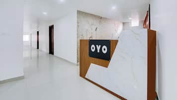 Un área de recepción con un mostrador de mármol, una pared con un mural de temática natural y un pasillo con puertas.