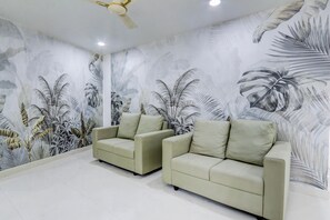 A room with two beige sofas, a ceiling fan, and a wall with a tropical leaf pattern. - Hotel O Viraj Luxury Stay (Warangal)