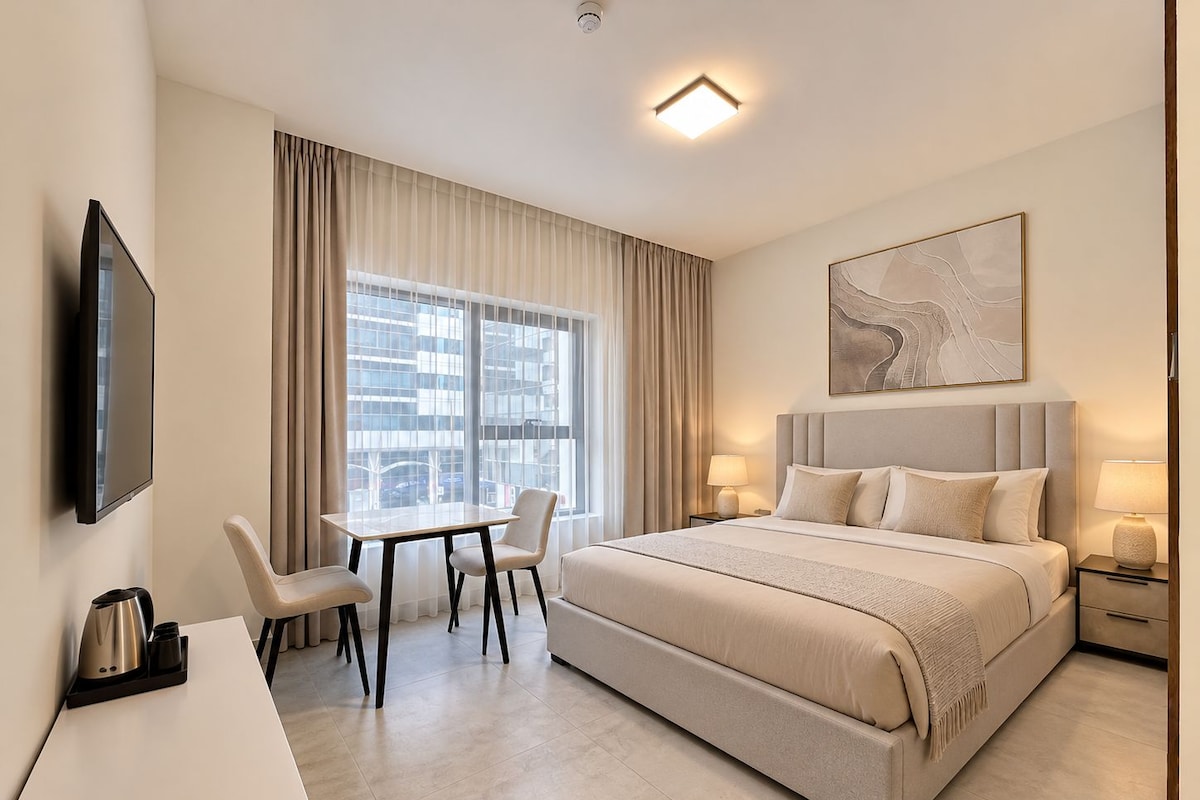A hotel room with a bed, a desk, chairs, a TV, and a window with curtains.
