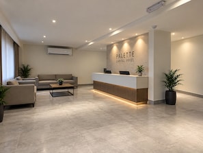 A modern hotel reception area with a reception desk, sofas, and potted plants. - Palette Capital Hotel (Abu Dhabi)