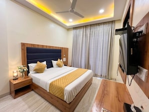 A hotel room with a bed, bedside table, lamp, curtains, and a television. - National Hotel (Mumbai)