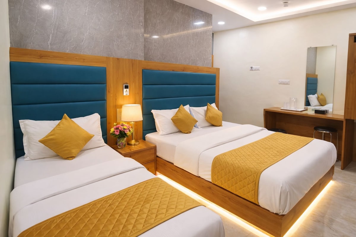 A hotel room with two beds, a wooden headboard, a bedside table with a lamp, and a mirror.