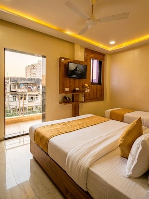 A hotel room with a bed, a television mounted on a wooden panel, and a balcony with a city view. - National Hotel (Mumbai)