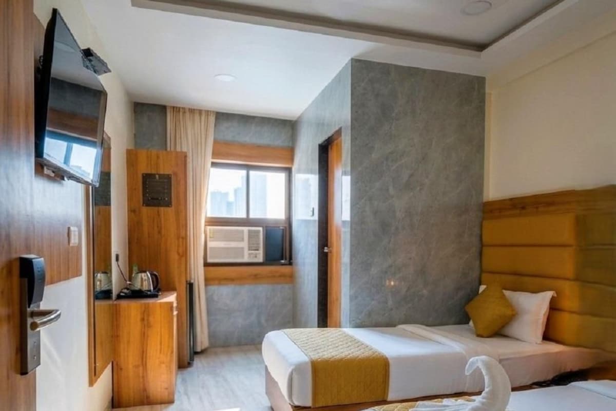 A hotel room with two beds, a wooden wardrobe, a television, and a window with curtains.