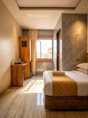 A hotel room with a bed, a wooden desk, a window with curtains, and a stone wall. - National Hotel (Mumbai)