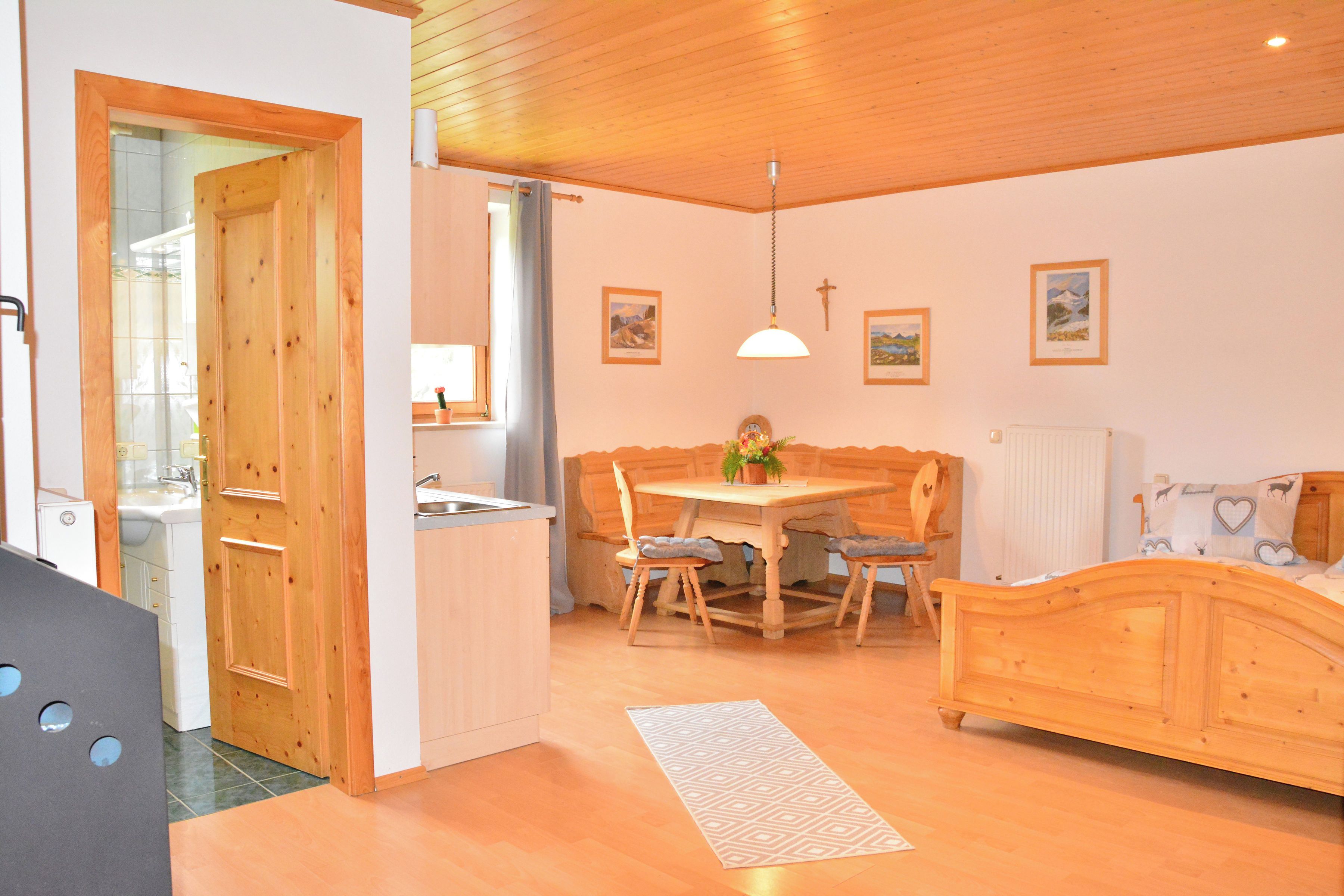 A cozy room with a wooden dining table, a bed, and a kitchen area.