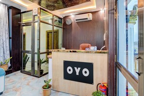 Bancada de recepção com placa indicando 'OYO', em interior moderno com painéis de madeira e entrada por porta de vidro.