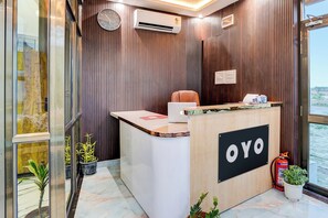Balcão de recepção com uma placa indicando 'OYO' e um laptop em cima. Há um extintor de incêndio e uma janela com vista para o exterior.