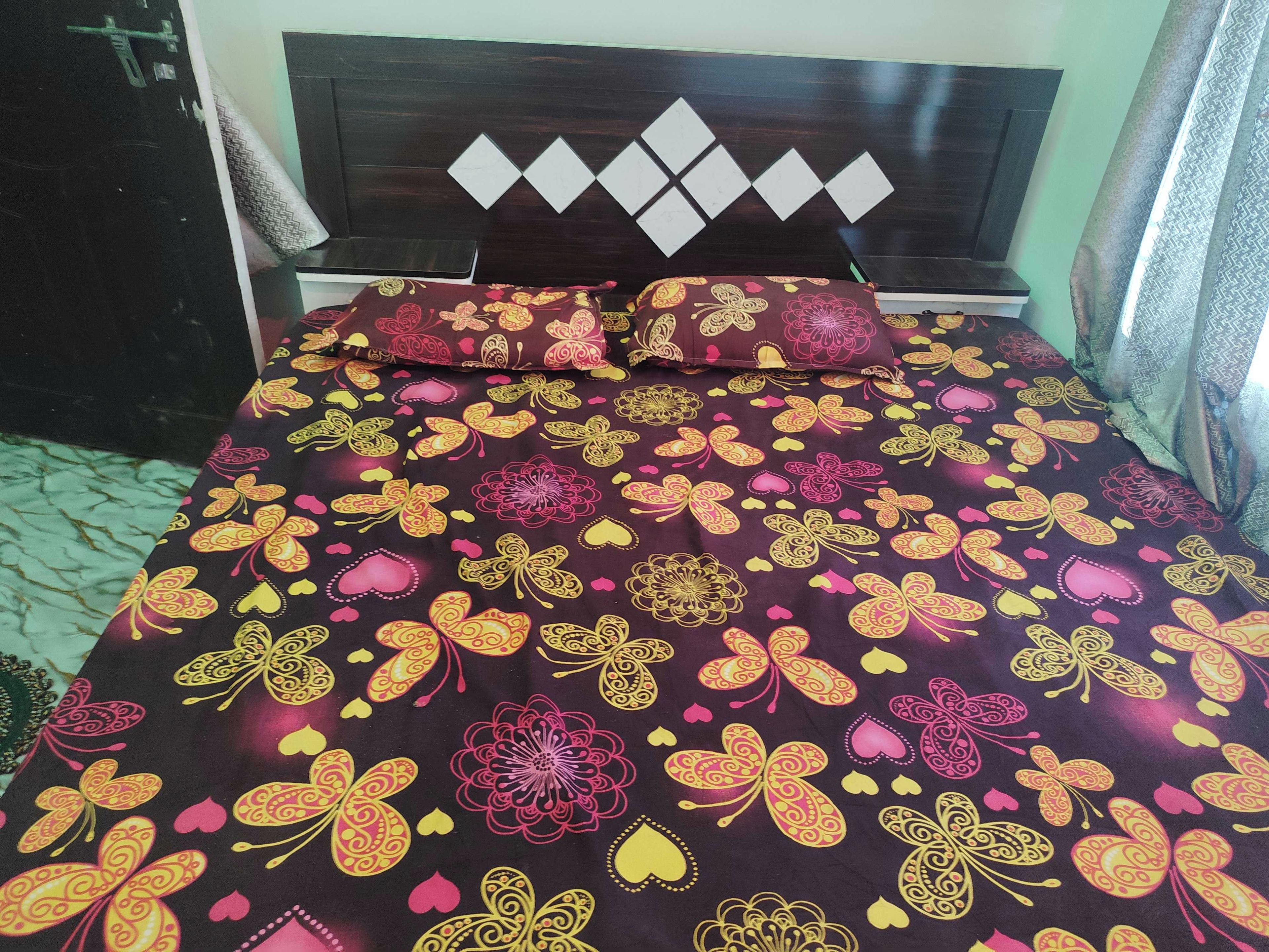 A bed with a patterned bedspread and two pillows, a dark wooden headboard with diamond-shaped decorations, and a green wall.