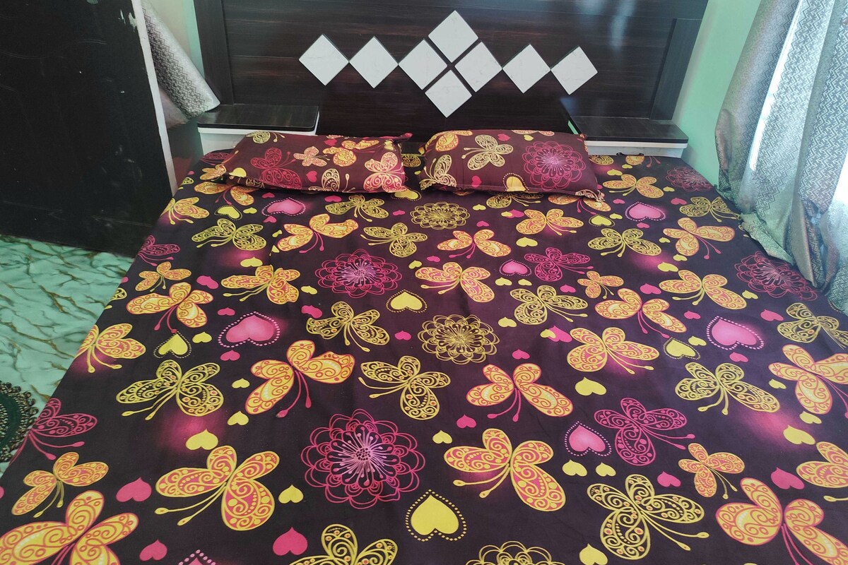 A bed with a patterned bedspread and two pillows, a dark wooden headboard with diamond-shaped decorations, and a green wall.