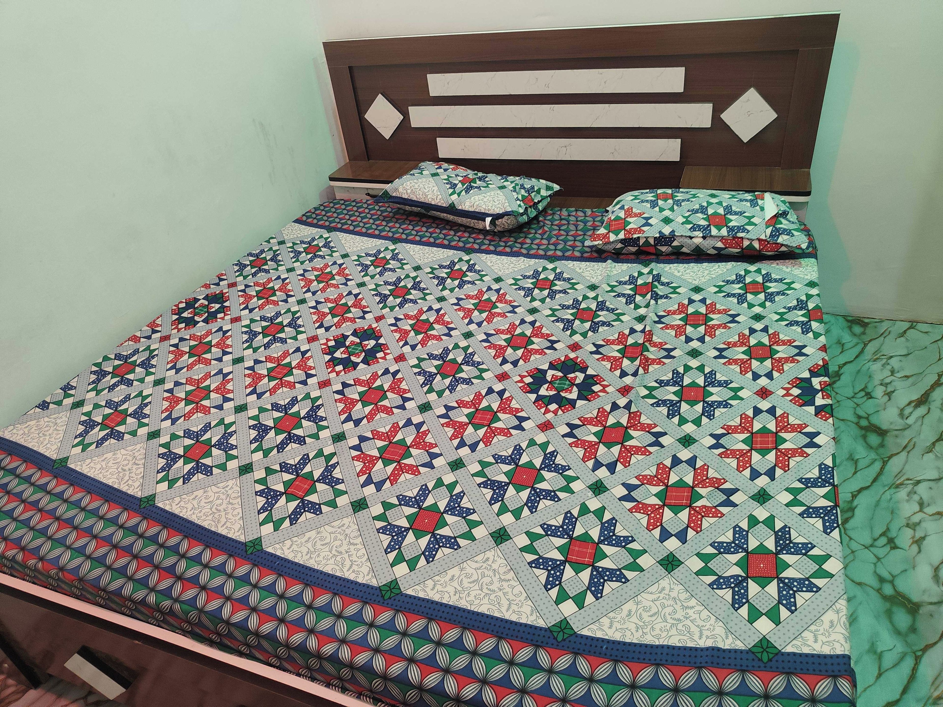 Een bed met een quilt met patroon en kussens, een houten hoofdbord en een nachtkastje.