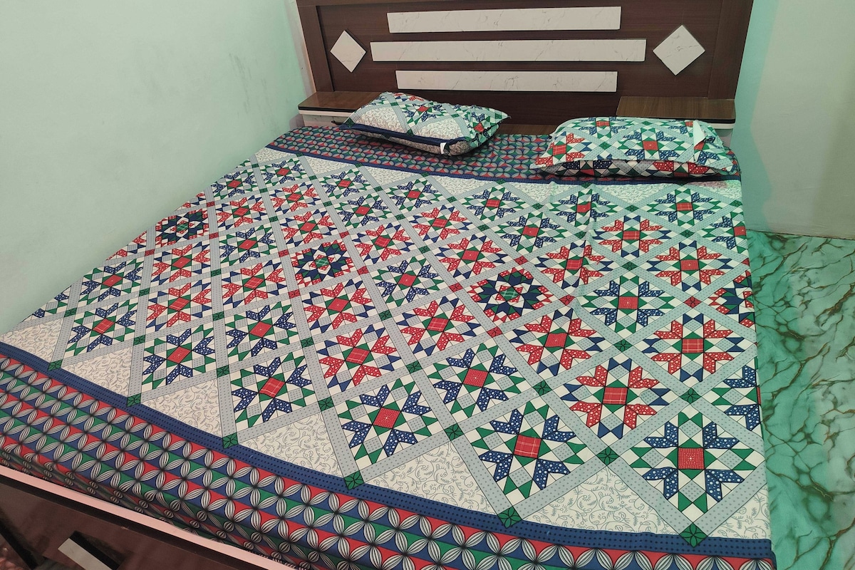 A bed with a patterned quilt and pillows, a wooden headboard, and a bedside table.