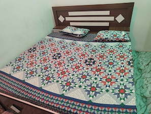 A bed with a patterned quilt and pillows, a wooden headboard, and a bedside table.