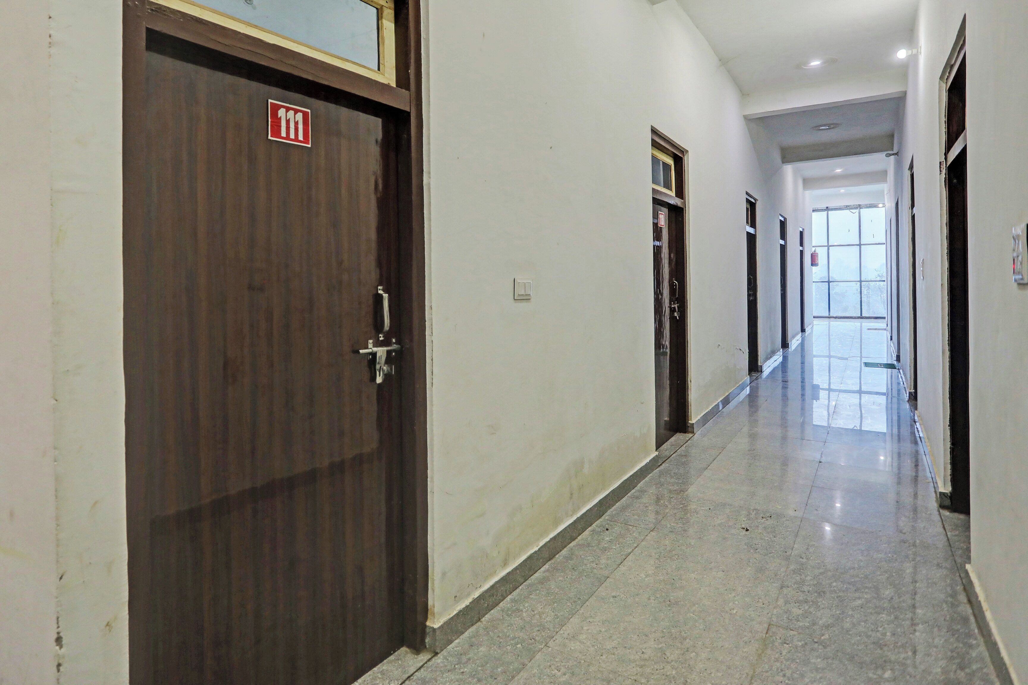 Un pasillo con puertas de madera, un letrero de salida de emergencia y un extintor.