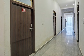 A corridor with wooden doors, a fire exit sign, and a fire extinguisher. - Hotel O THE KING HEAVEN (Bhongaon)