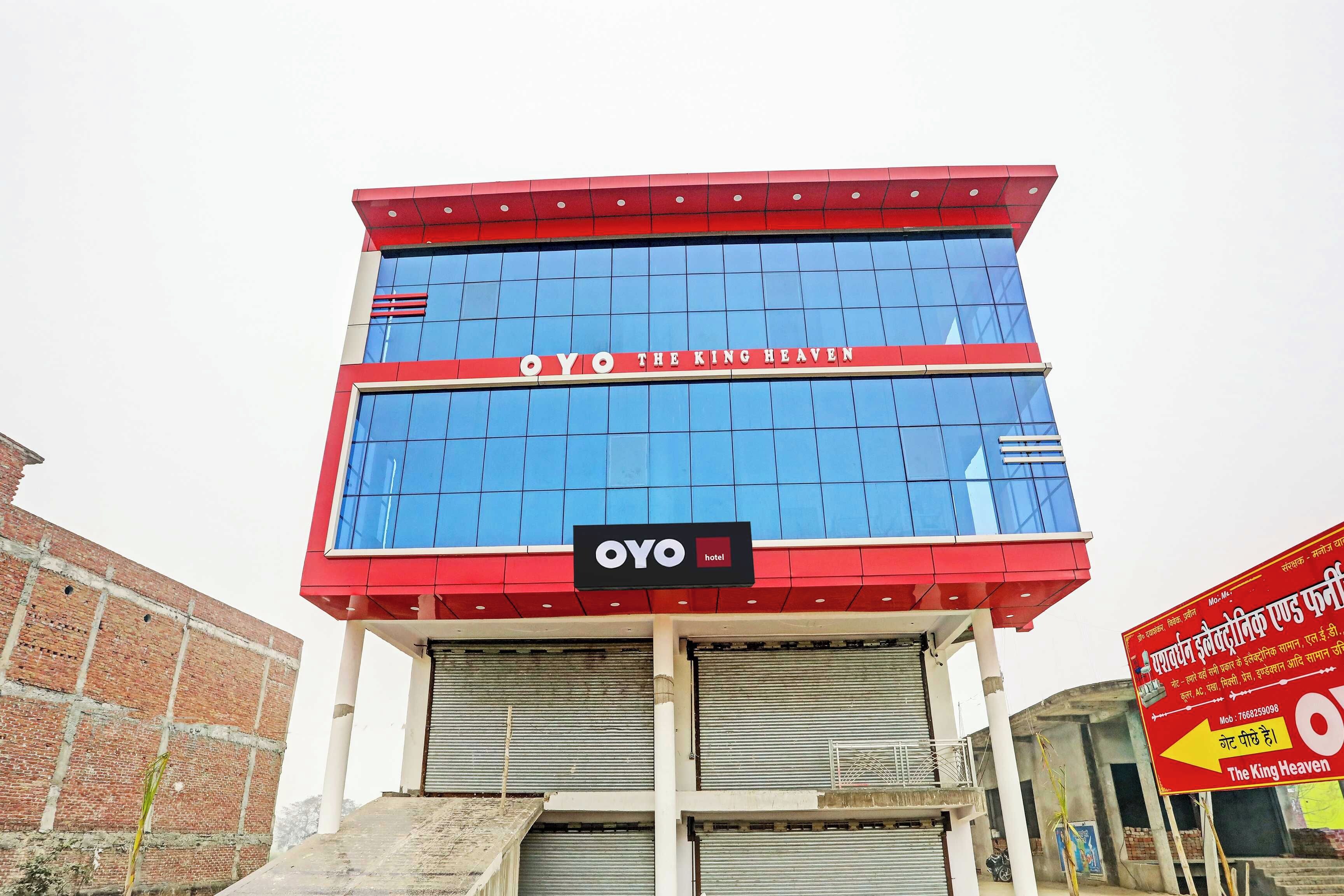 A hotel building with a red and blue facade, a sign reading 'OYO THE KING HEAVEN', and a signboard with hotel name in Hindi.