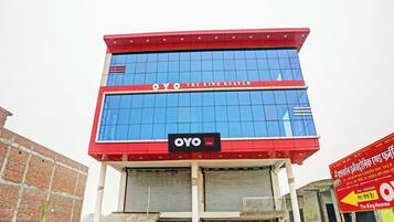 A hotel building with a red and blue facade, a sign reading 'OYO THE KING HEAVEN', and a signboard with hotel name in Hindi.