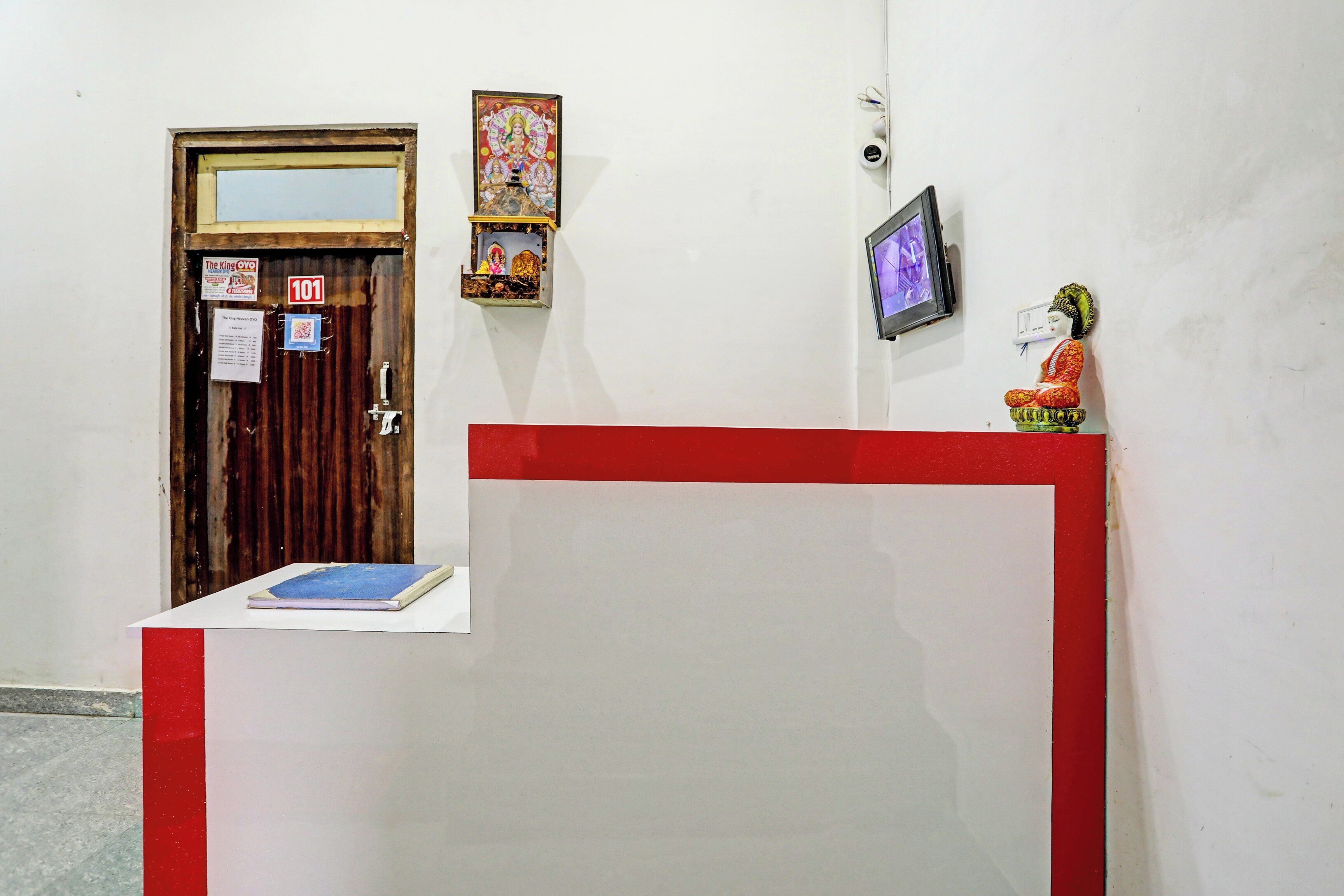 Un área de recepción con una puerta de madera, un pequeño santuario, un cuadro enmarco y un televisor montado en la pared.