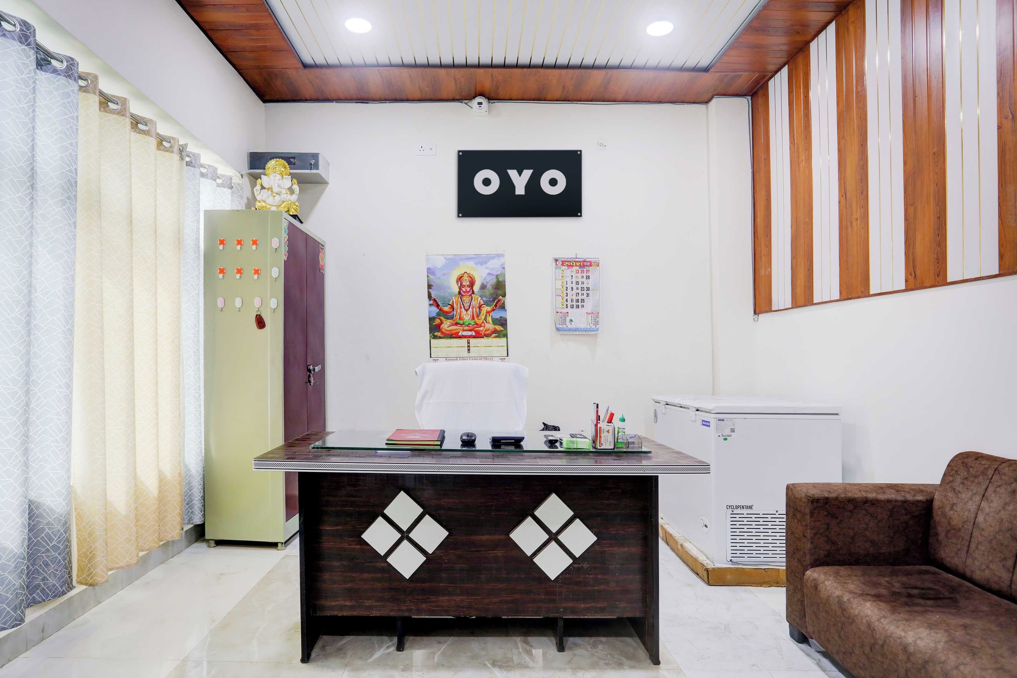 Un comptoir d’accueil en bois foncé, orné de découpes en forme de losange, un réfrigérateur, un panneau mural portant l’inscription « OYO », un calendrier et un canapé marron.