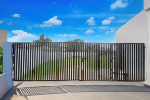 A metal gate with vertical bars, a clear sky, and a view of a green area beyond. - Hotel O by OYO Aparna and Marriage Lawn (Balrampur)