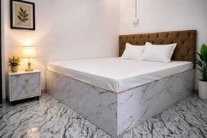 A bed with a marble base, a nightstand with a lamp, and a plant. - Hotel O Mahi Palace (Bisalpur)