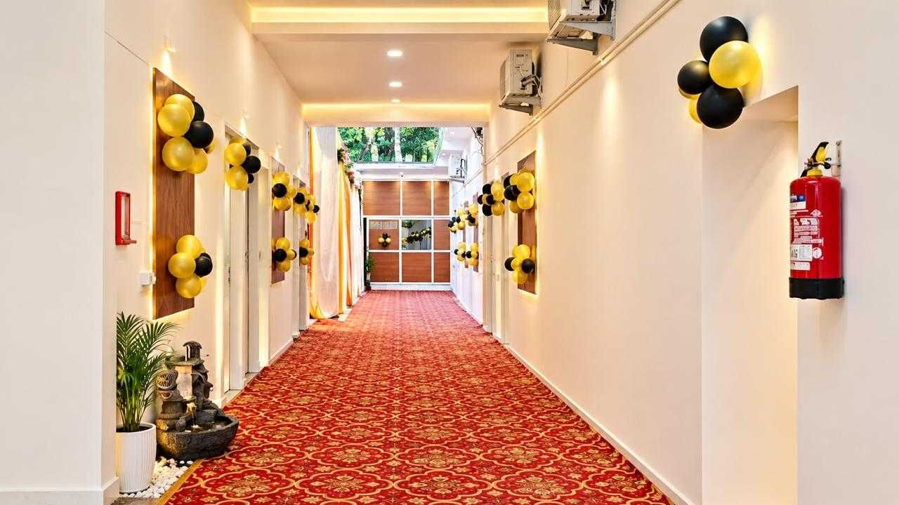 A hotel corridor with a red carpet, walls adorned with black and yellow balloons, and a fire extinguisher mounted on the wall.
