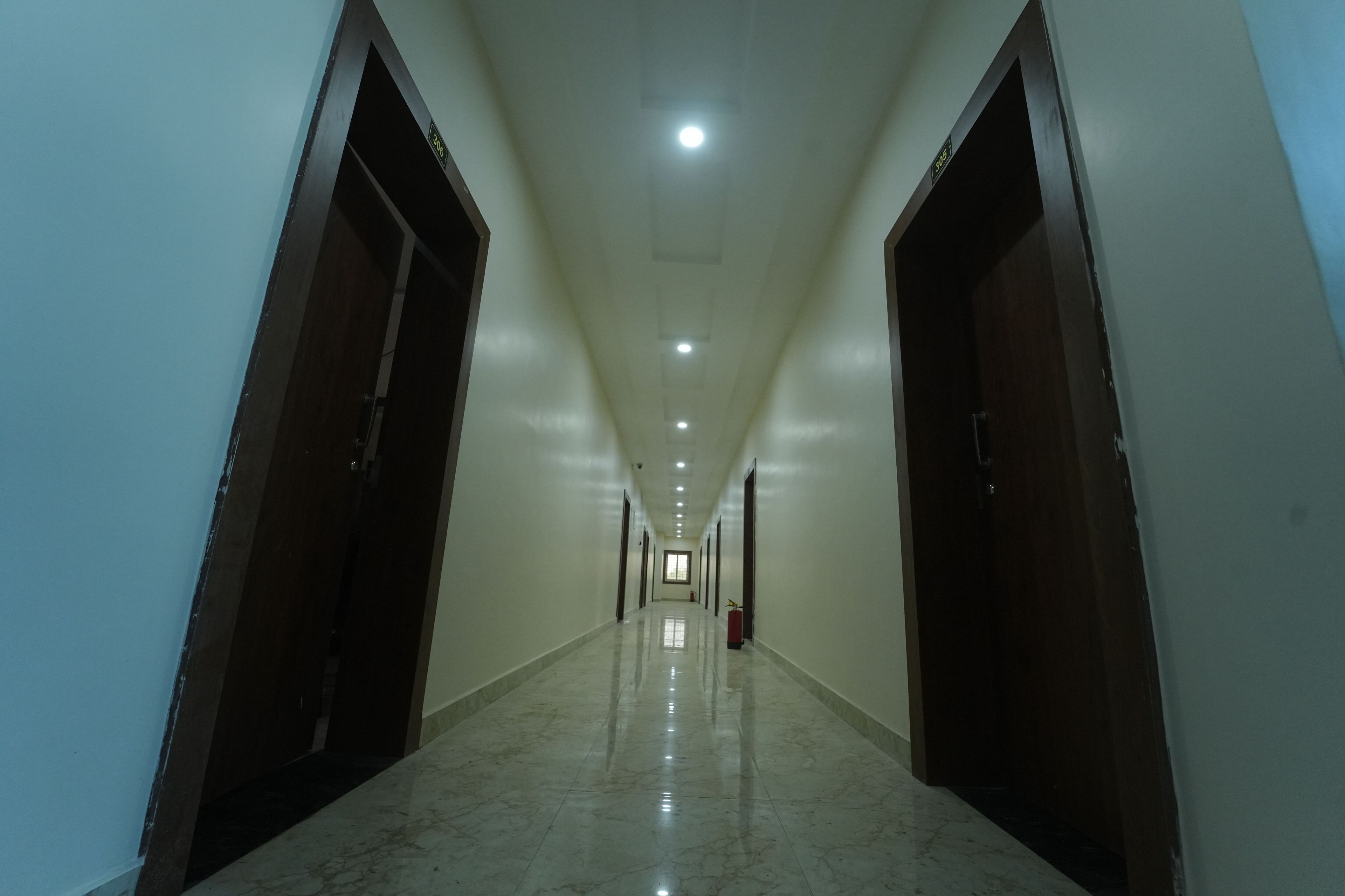 Un pasillo largo y estrecho con puertas a ambos lados y un extintor en la pared derecha.