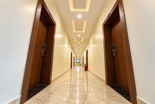 A hotel hallway with wooden doors, marble flooring, and recessed lighting.