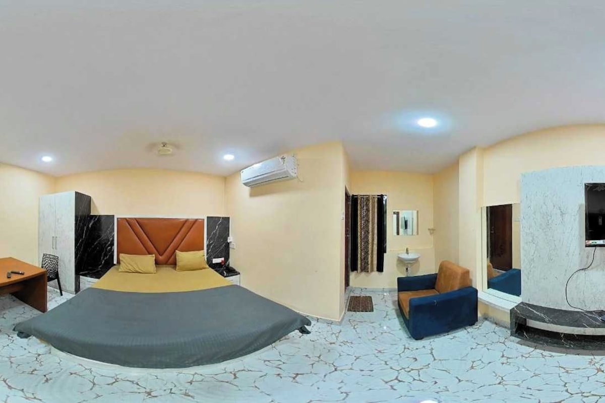 A hotel room with a bed, a desk, a chair, a TV, and an air conditioning unit.
