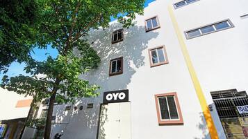 A building with multiple windows, a sign reading 'OYO', and a tree in the foreground.