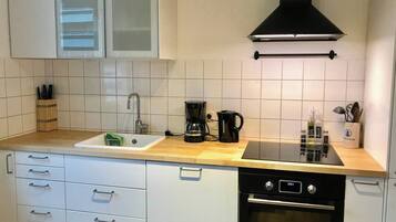 Une cuisine avec des meubles blancs, une cuisinière noire, une machine à café et un évier.