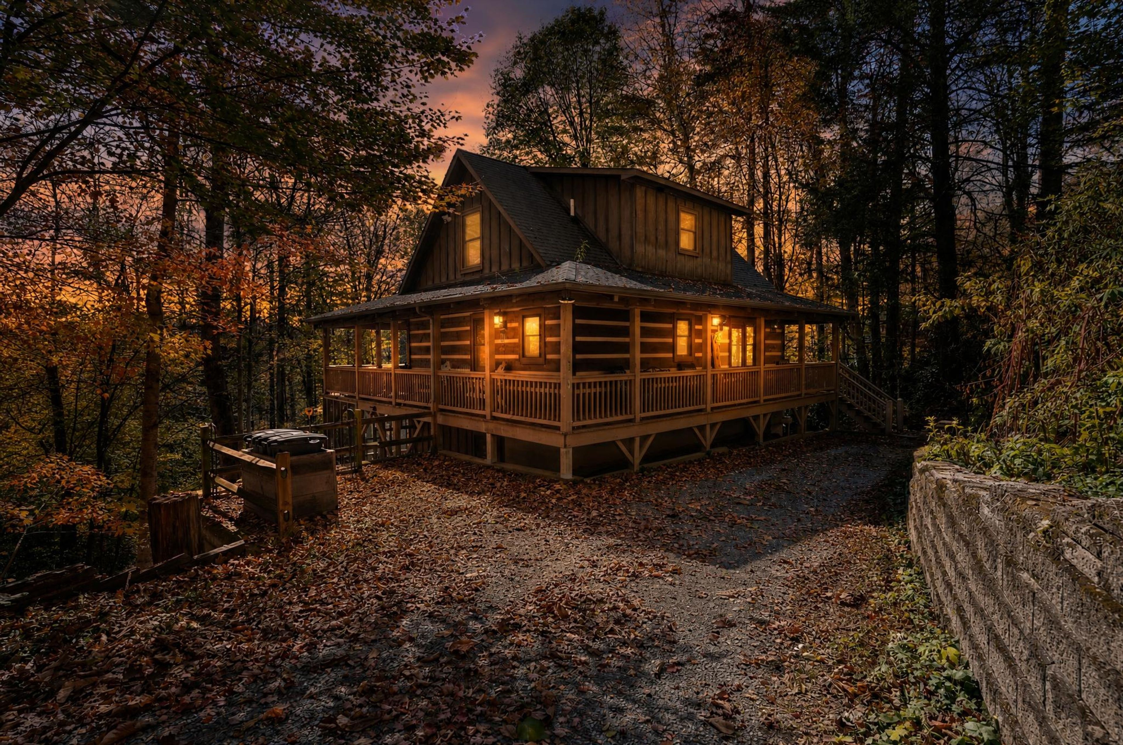 Exterior dusk view of a woodland log cabin with illuminated wrap-around porch.
