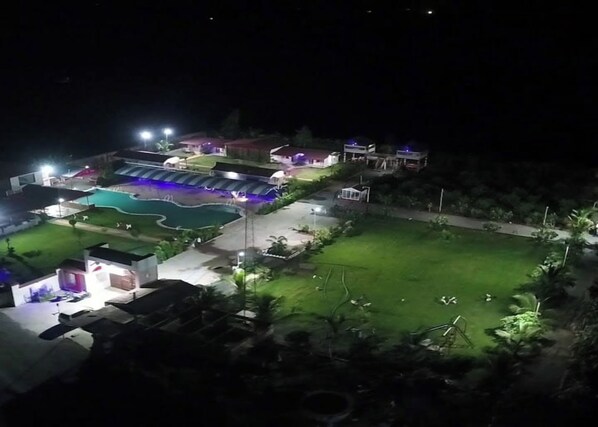 A residential area with multiple houses, a swimming pool, and a well-lit lawn.