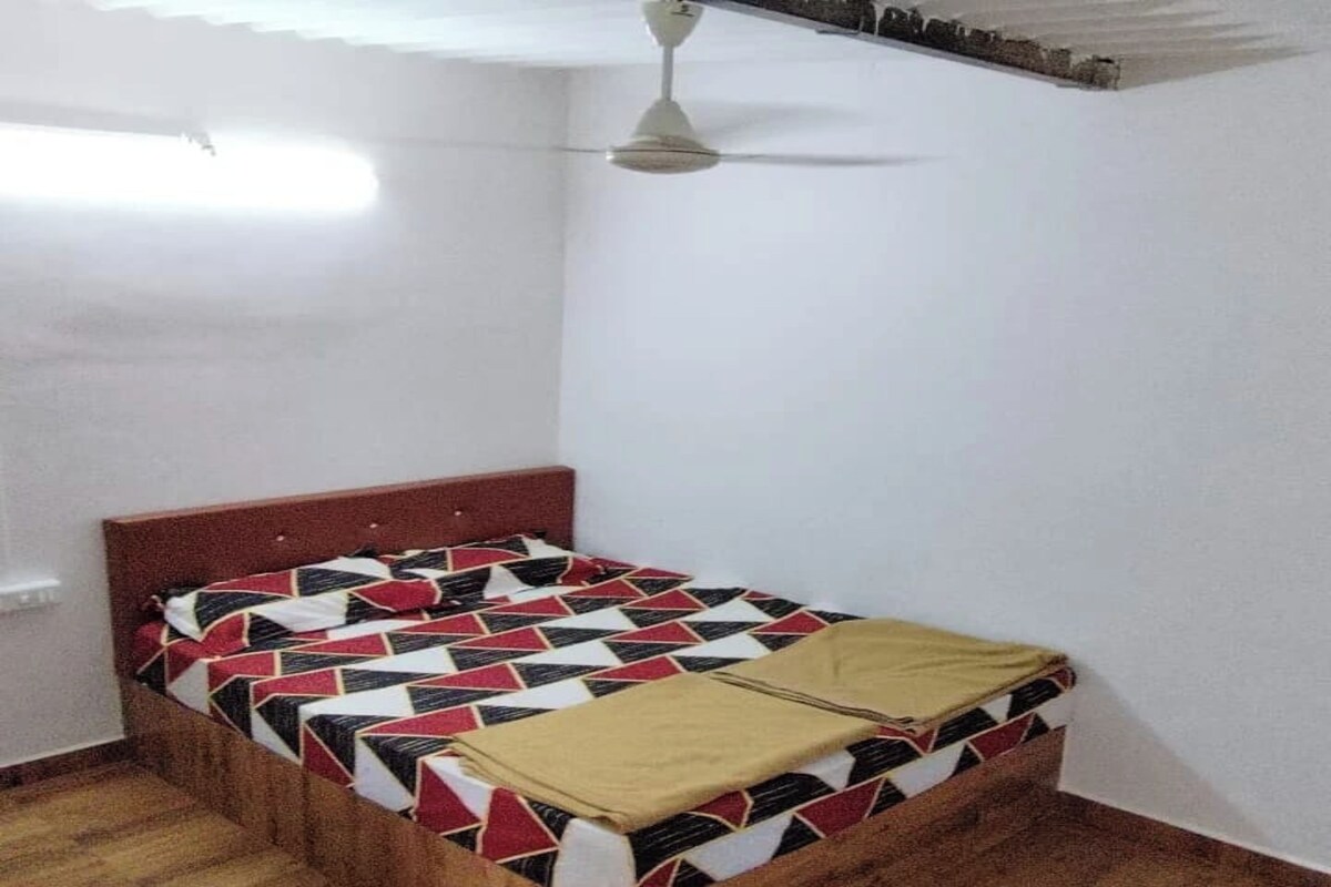 Un lit simple avec une couvre-lit à motifs géométriques, une tête de lit en bois et un ventilateur de plafond.