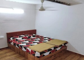 Un lit simple avec une couvre-lit à motifs géométriques, une tête de lit en bois et un ventilateur de plafond.
