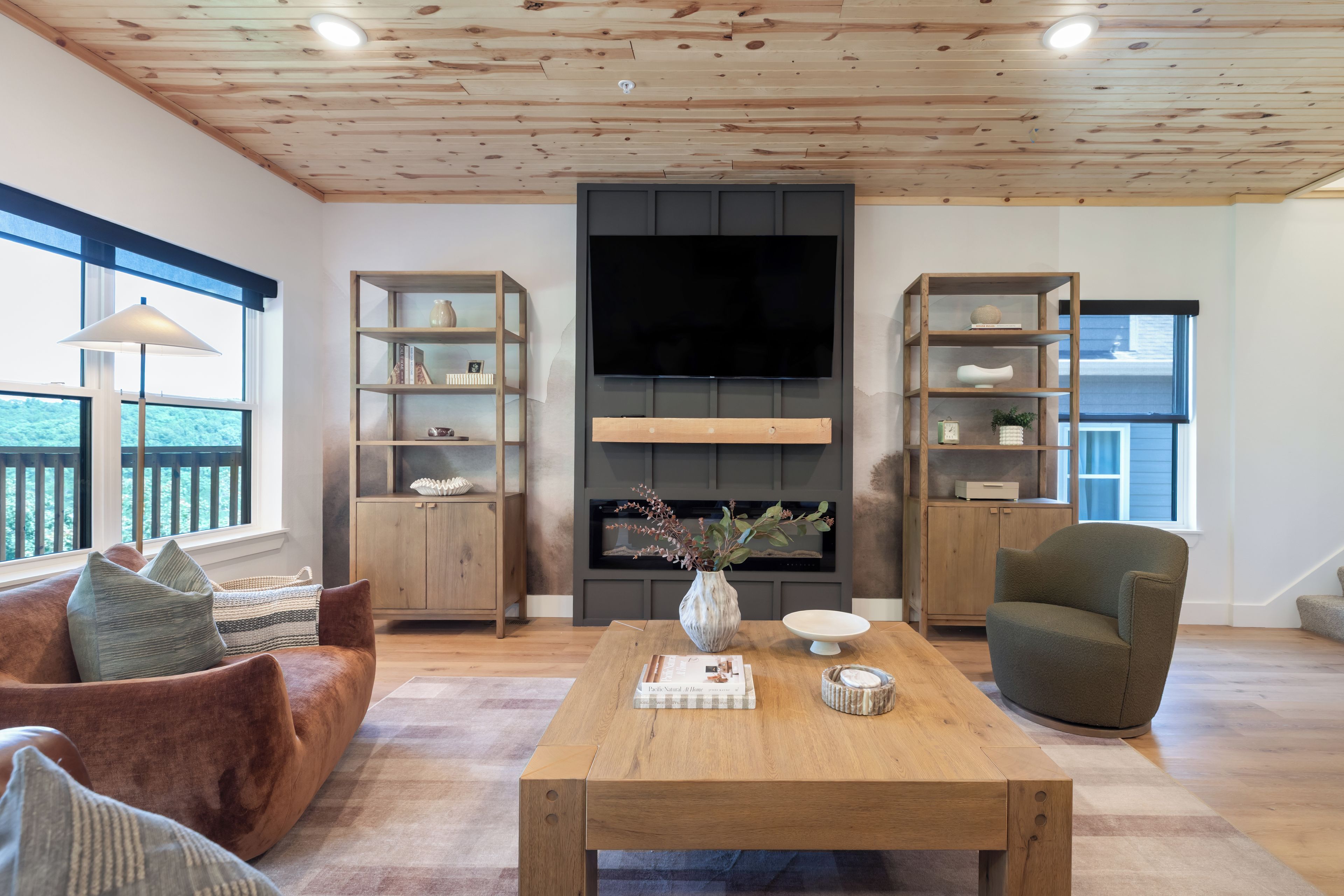 A modern living room with a wooden ceiling, built-in shelving, a flat-screen TV, a fireplace, and a comfortable seating area.