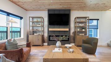 A modern living room with a wooden ceiling, built-in shelving, a flat-screen TV, a fireplace, and a comfortable seating area.
