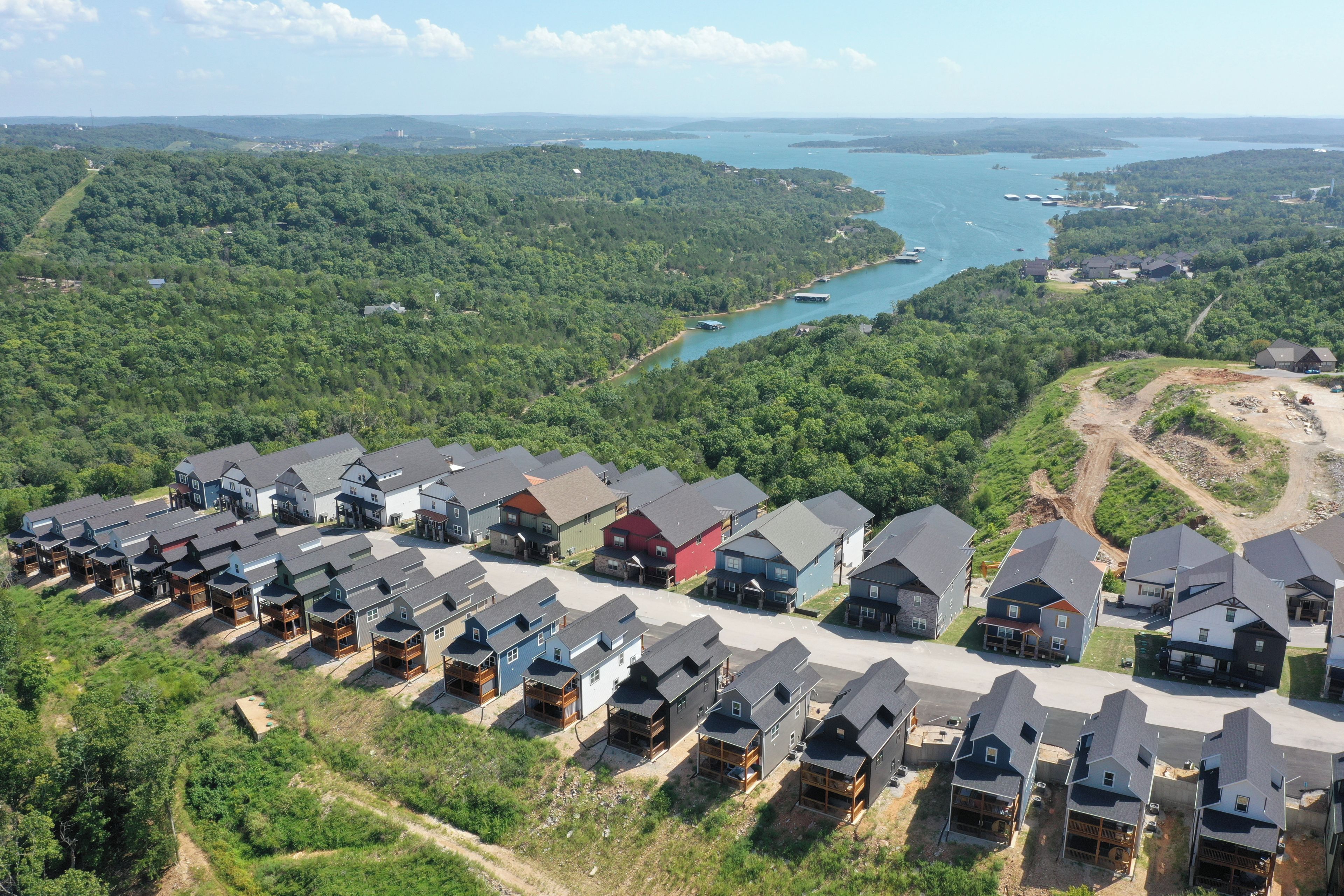 A residential area with multiple houses, a clear view of a lake, and a forested landscape.
